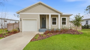 Une maison de plain-pied avec un garage, une porte d’entrée et un petit jardin devant la maison, avec de la pelouse et du paillis.