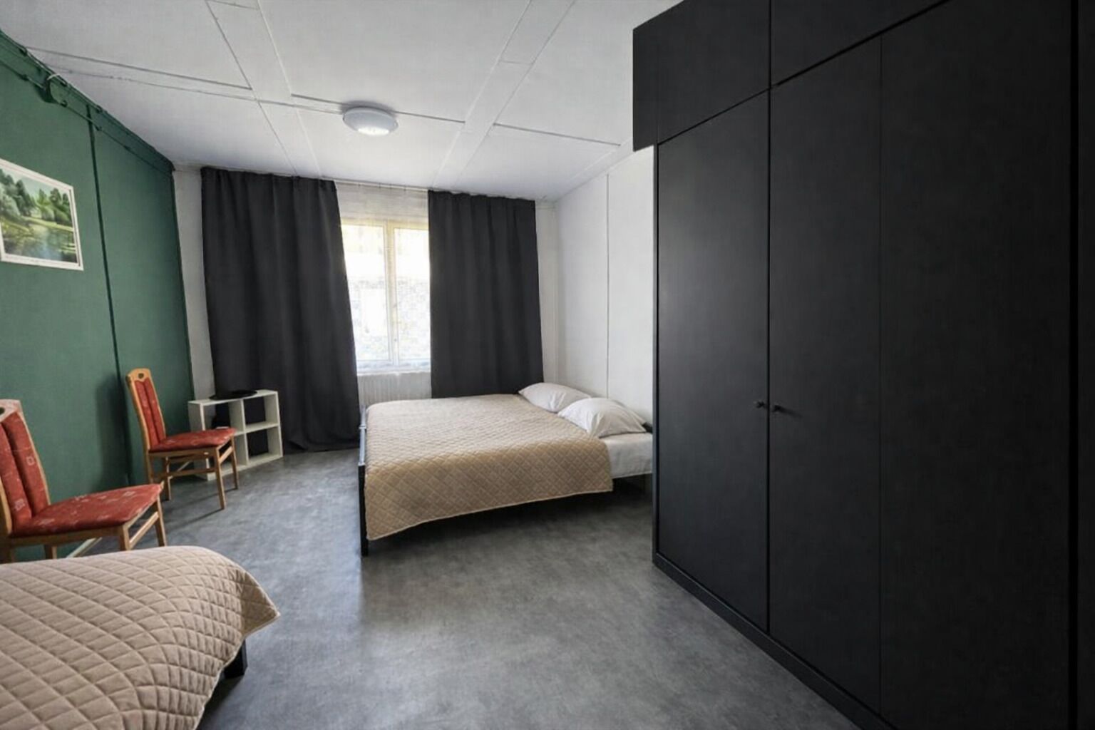 A bedroom with a bed, a chair, a wardrobe, and a window with curtains.