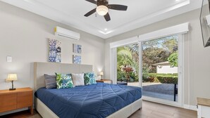 A bedroom with a large bed, a ceiling fan, an air conditioning unit, and a view of a garden through a sliding glass door. - Casa 17 at The Point // Playa Avellanas // 25 min to Tamarindo (Playa Avellanas)