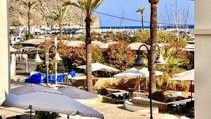 A seaside patio with outdoor seating, palm trees, and a view of boats and the sea. - Boho Luxury Apartment · Moraira Centre THE MORAIRA COLLECTION - 2 (Moraira)
