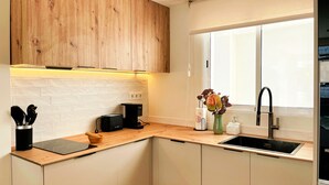 A modern kitchen with wooden cabinets, a black countertop, a coffee machine, and a sink. - Boho Luxury Apartment · Moraira Centre THE MORAIRA COLLECTION - 2 (Moraira)