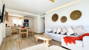 A modern living room with a white sofa, wooden coffee table, and a dining area with a wooden table and chairs. - Boho Luxury Apartment · Moraira Centre THE MORAIRA COLLECTION - 2 (Moraira)