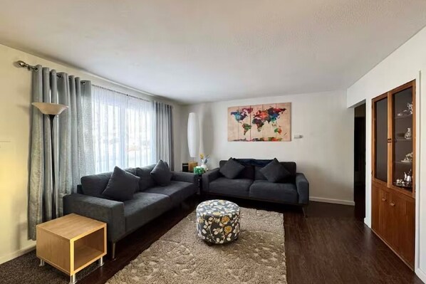 Ein Wohnzimmer mit zwei grauen Sofas, einem runden Hocker, einem Holztisch und einem Wandbild einer Weltkarte.