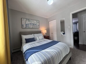 A bedroom with a bed, a nightstand, a lamp, a wardrobe, and a painting on the wall. - Aurora Hideaway (Fairbanks)