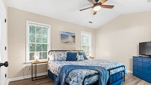 A bedroom with a bed, a ceiling fan, a TV, and a dresser. - Experience Oak Island at Stitch by the Sea, a cozy 3-bedroom retreat for 10. (Oak Island)