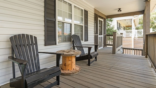 A covered porch with two Adirondack chairs and a small wooden table. - Experience Oak Island at Stitch by the Sea, a cozy 3-bedroom retreat for 10. (Oak Island)