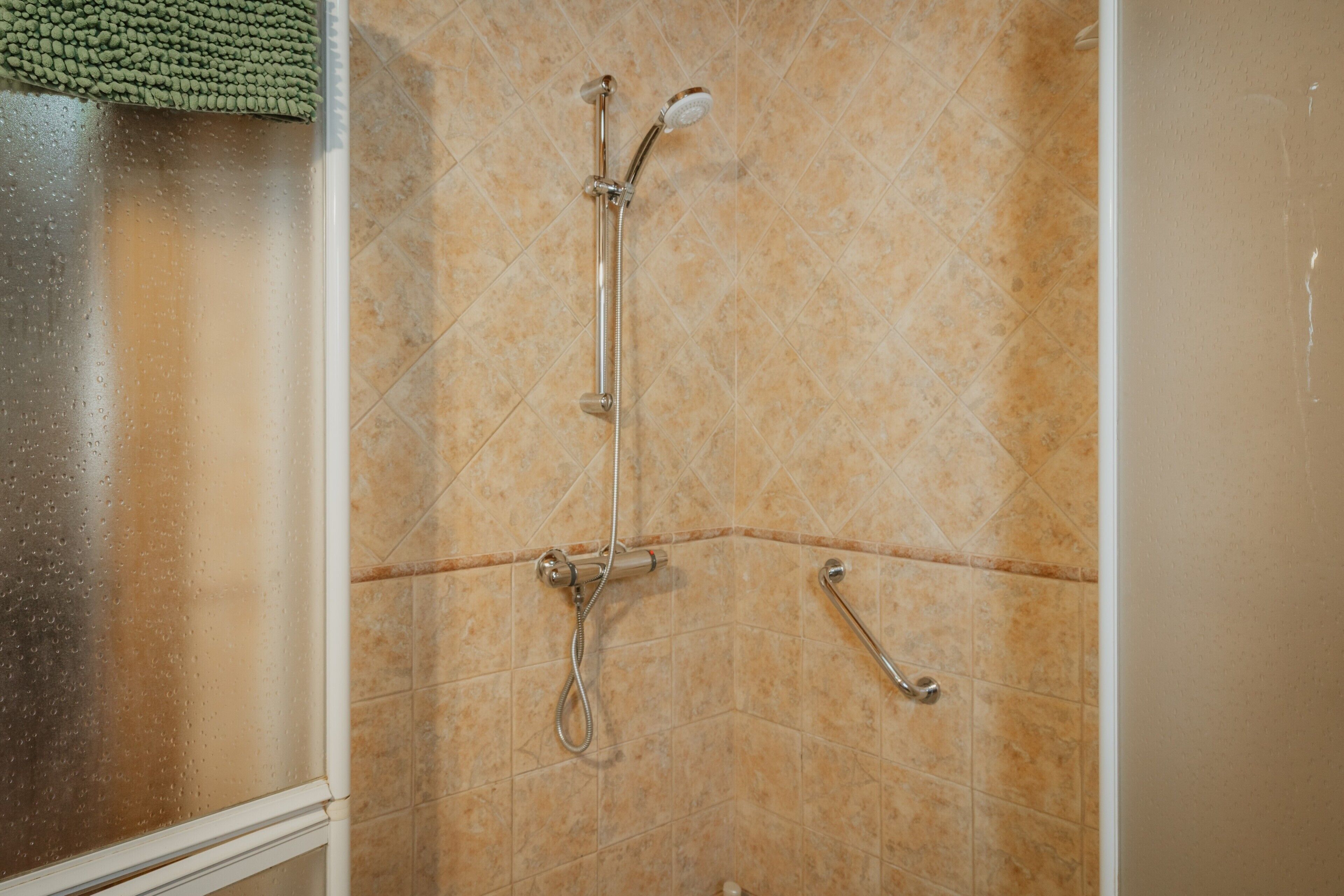 Une douche équipée d’un pommeau de douche à main et d’un robinet fixé au mur.