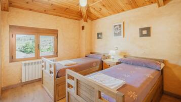 Una habitación con dos camas de madera, ventilador de techo, ventana con vistas y radiador.