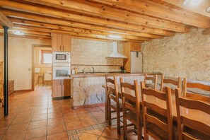 A kitchen with wooden cabinets, a stone wall, and a tiled floor.