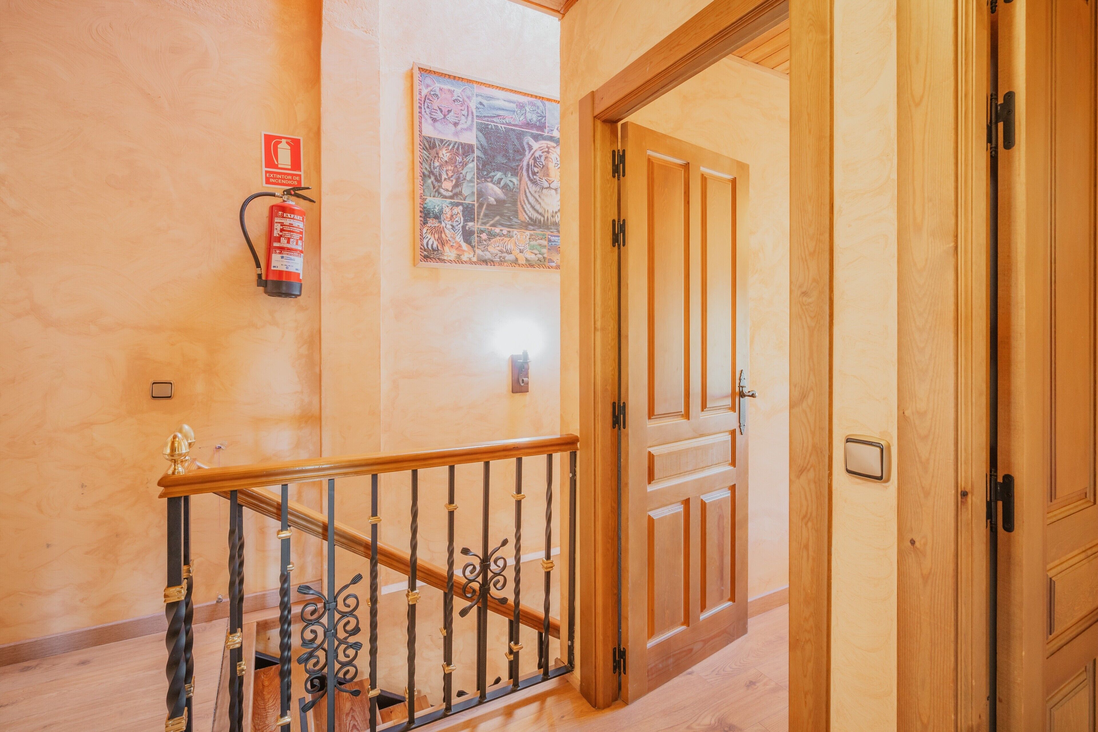Una escalera de madera con barandilla de metal, un extintor y una puerta que da a otra habitación.