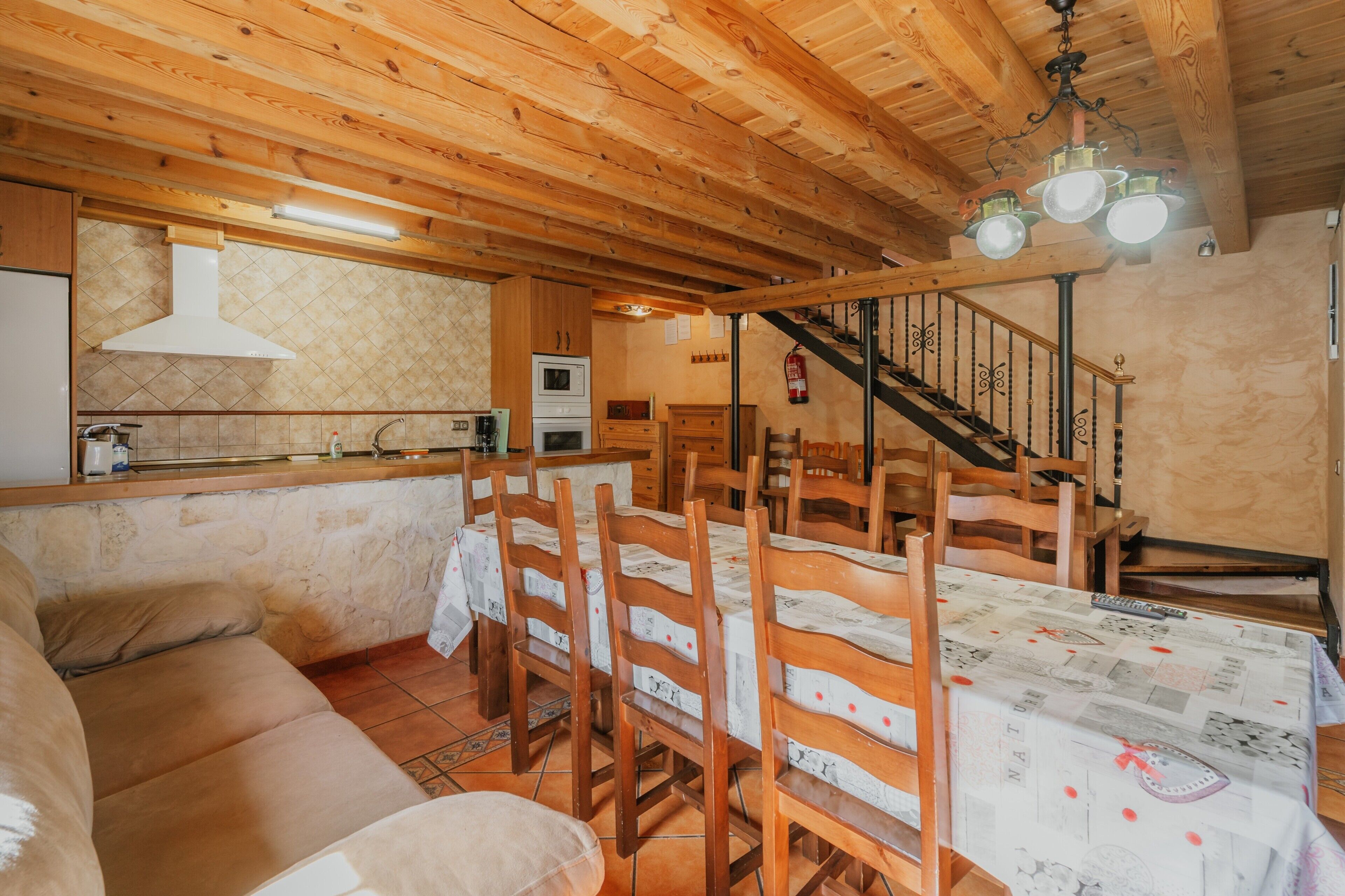 A wooden interior with a dining table, chairs, a sofa, a kitchen area, and a staircase.