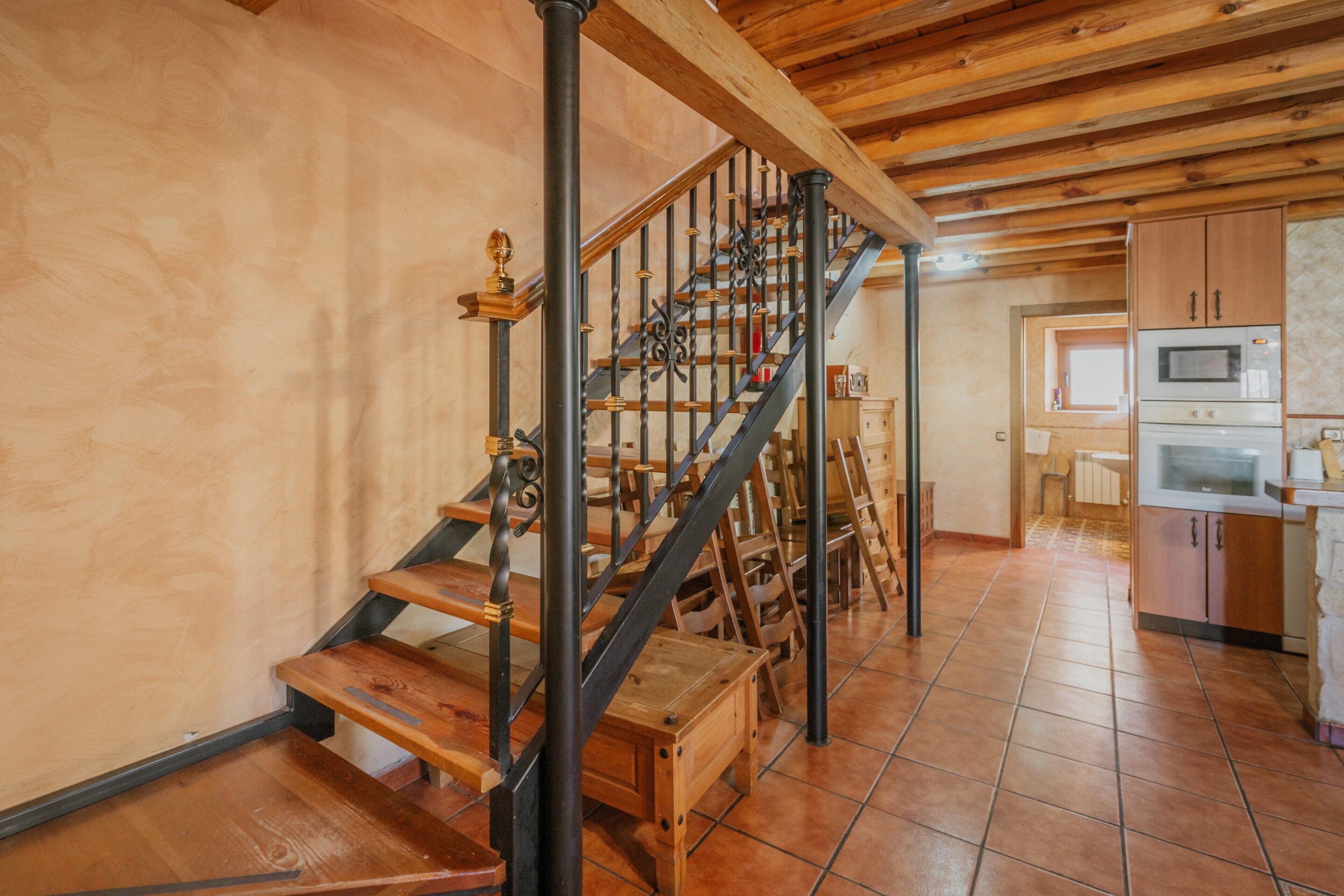 Una escalera de madera con barandillas de metal que lleva a una zona de cocina con armarios de madera y un microondas.