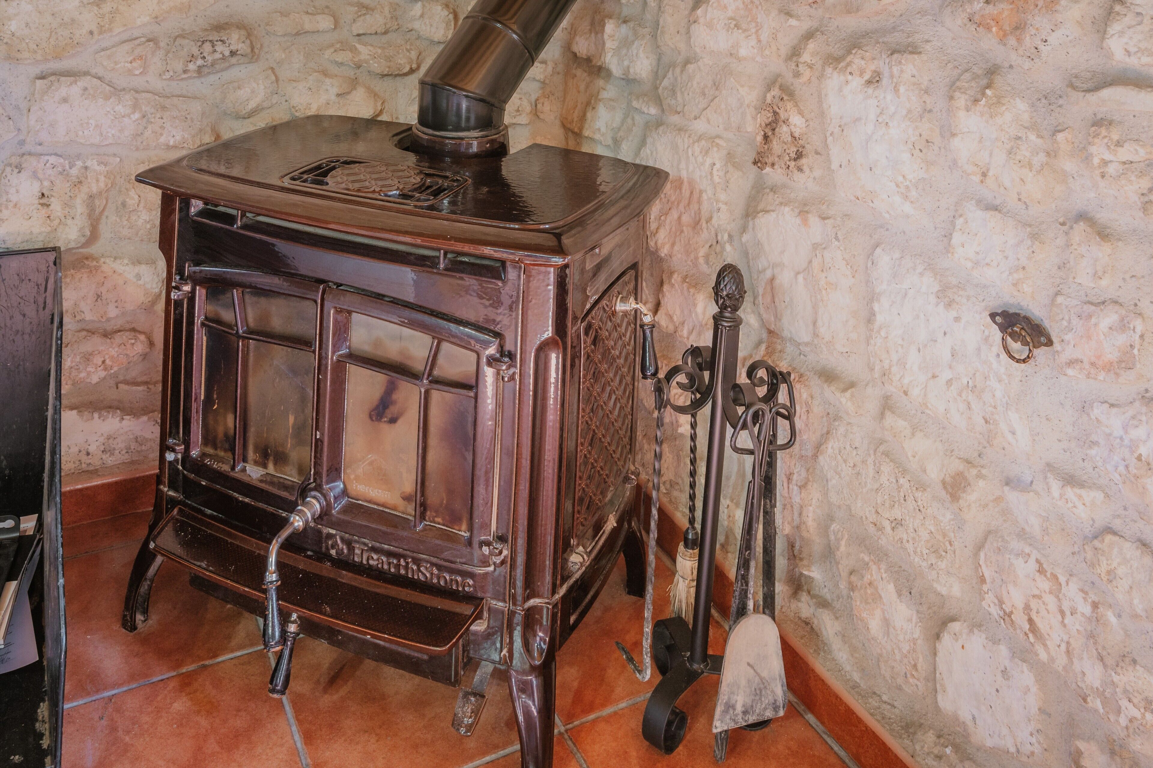 A vintage wood-burning stove with a chimney, set against a stone wall.