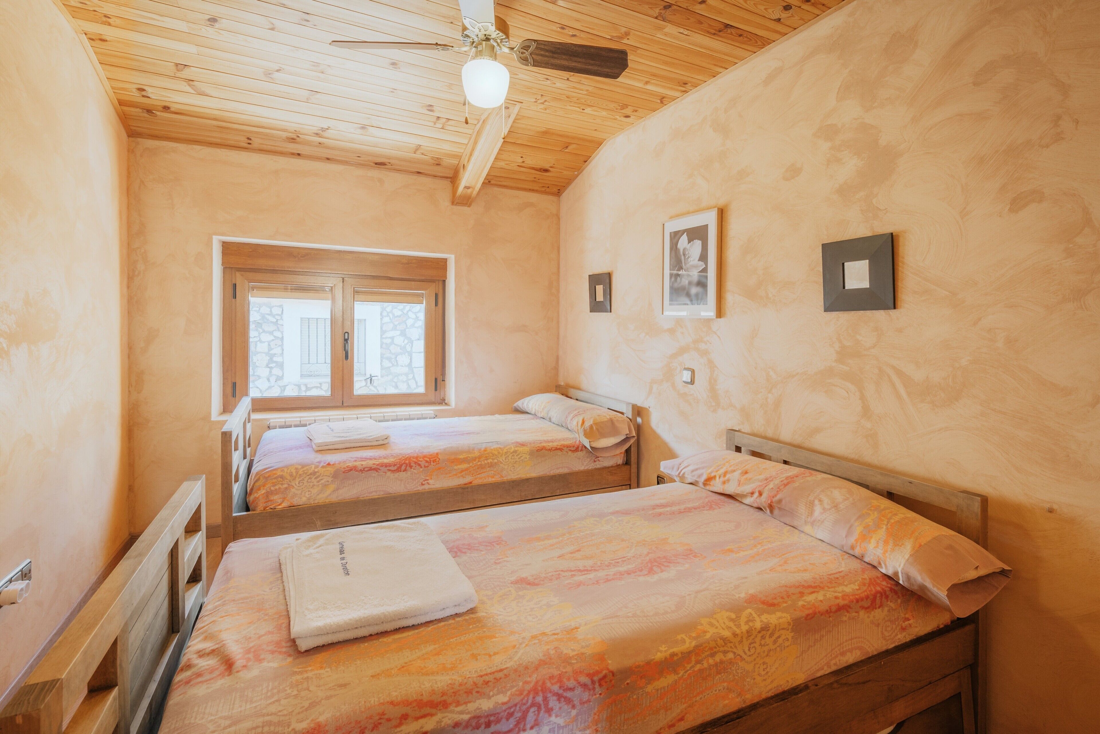 Ein Schlafzimmer mit zwei Holzbetten, einem Deckenventilator, einem Fenster und einer Tür.