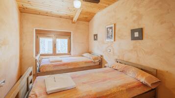 Ein Schlafzimmer mit zwei Holzbetten, einem Deckenventilator, einem Fenster und einer Tür.