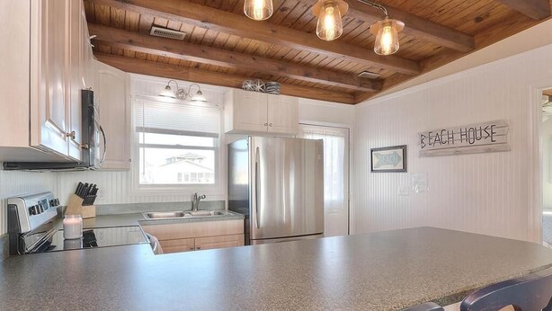 A kitchen with granite countertops, stainless steel appliances, wooden ceiling beams, and a 'Beach House' sign. - Experience oceanfront luxury at The Blue Fiddler in Oak Island, perfect for 10 guests! (Oak Island)