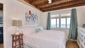 Een slaapkamer met een groot bed, een plafondventilator, een raam met gordijnen en een schilderij aan de muur.
