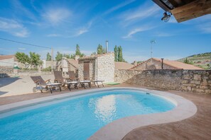 A swimming pool with lounge chairs, a stone structure, and a clear blue sky.