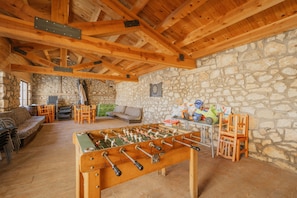 A room with a foosball table, stone walls, wooden beams, and a stone fireplace.