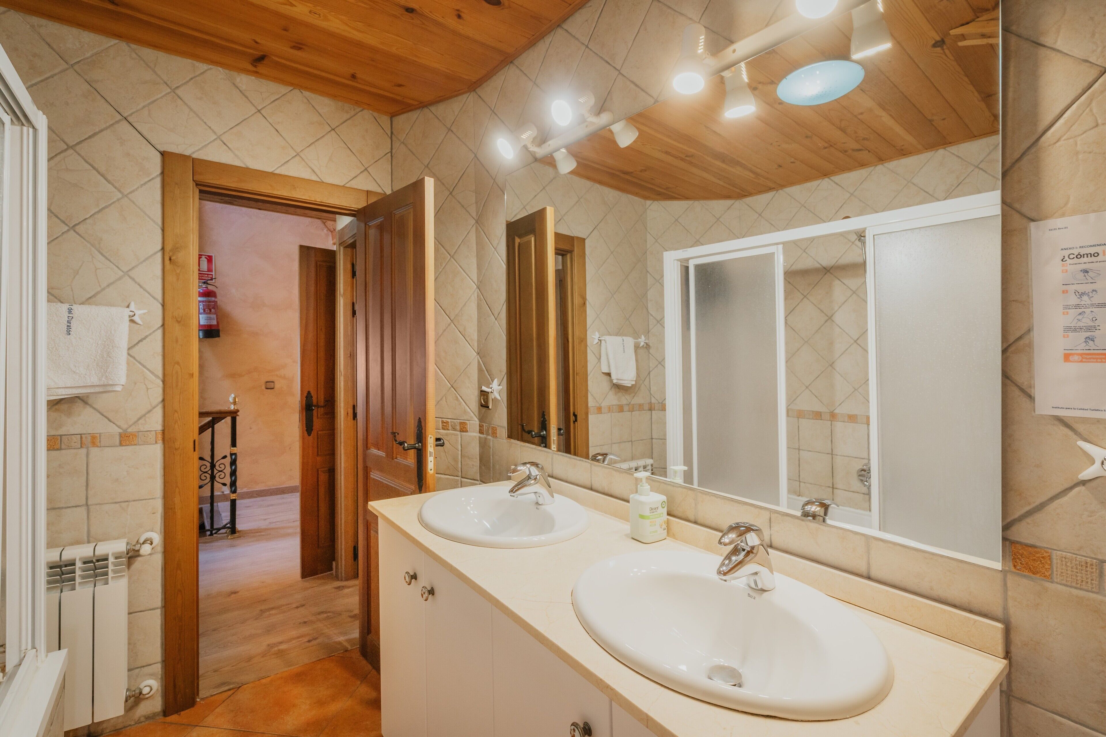 Un baño con dos lavamanos, techo de madera y un espejo grande.