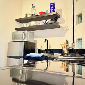 A kitchen with a microwave, refrigerator, and a shelf with various items. - Basilio Studio (Puerto Vallarta)