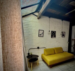 A room with a yellow sofa, a small round table, and a white brick wall with three framed pictures. - Basilio Studio (Puerto Vallarta)