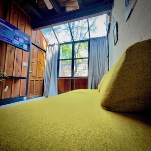 A room with a bed, wooden walls, a window with curtains, and a TV mounted on the wall. - Basilio Studio (Puerto Vallarta)
