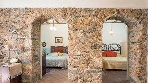 A room with a stone archway, a bed with a headboard, a bedside table, and a lamp.