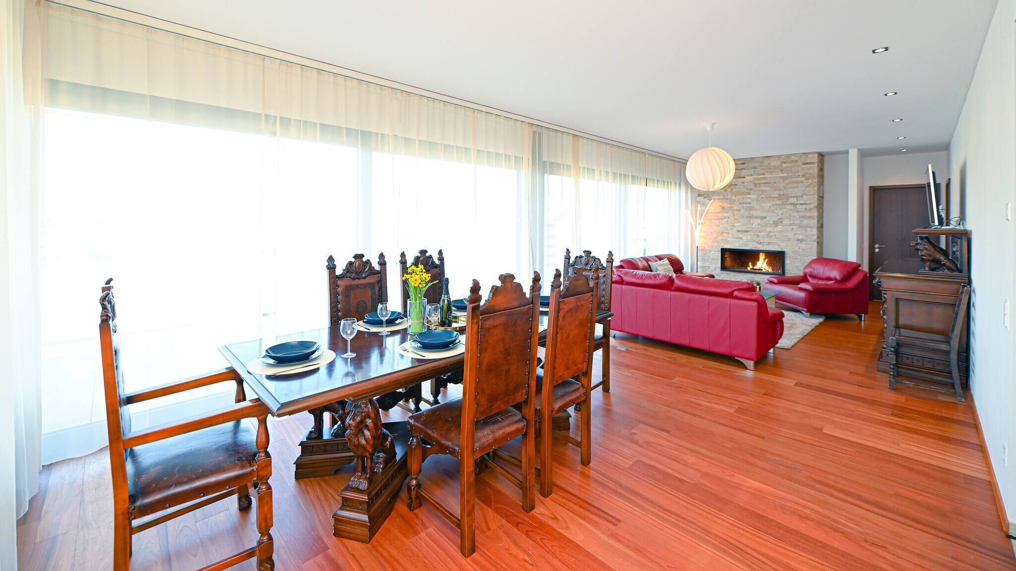Uma sala de jantar com mesa e cadeiras de madeira, um sofá vermelho e uma lareira.
