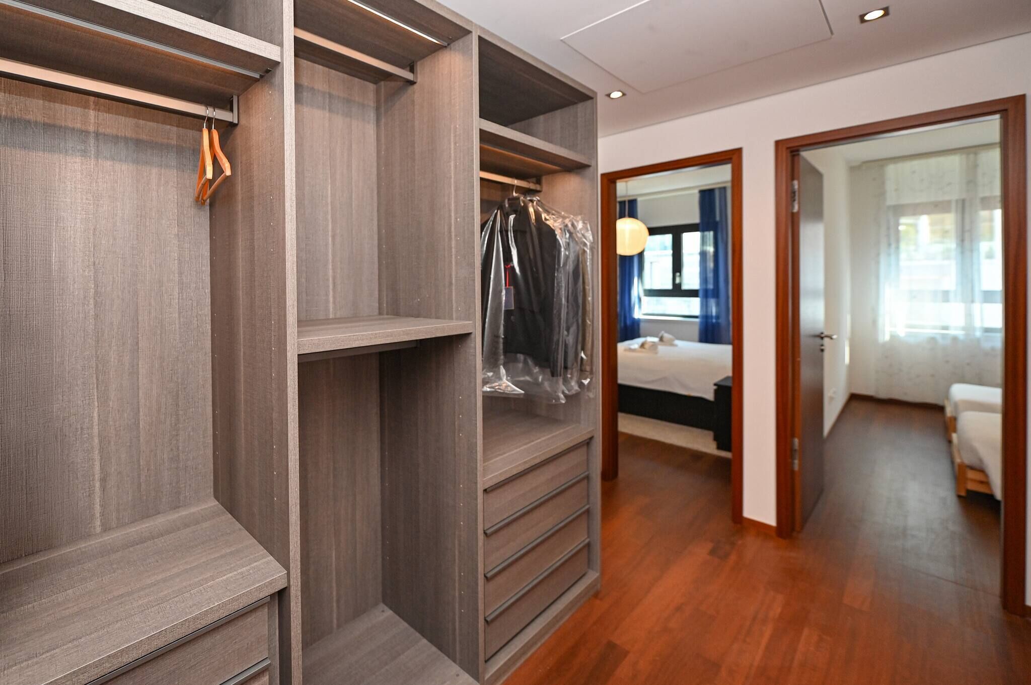 A hotel room with a wooden floor, a bed, a wardrobe, and a bathroom visible through an open door.