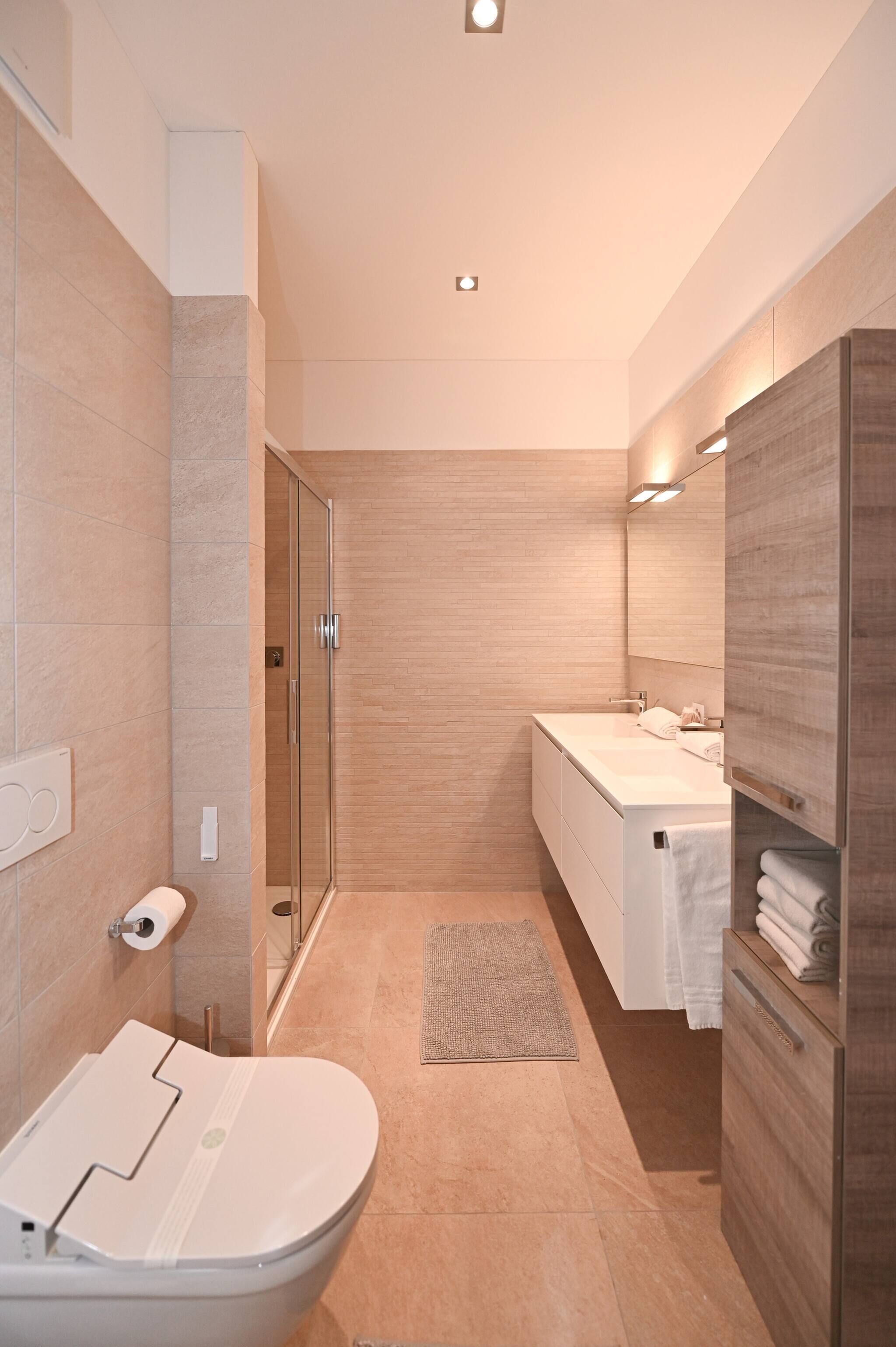 A modern bathroom with a glass shower enclosure, a white toilet, a sink with a mirror, and a wooden vanity.