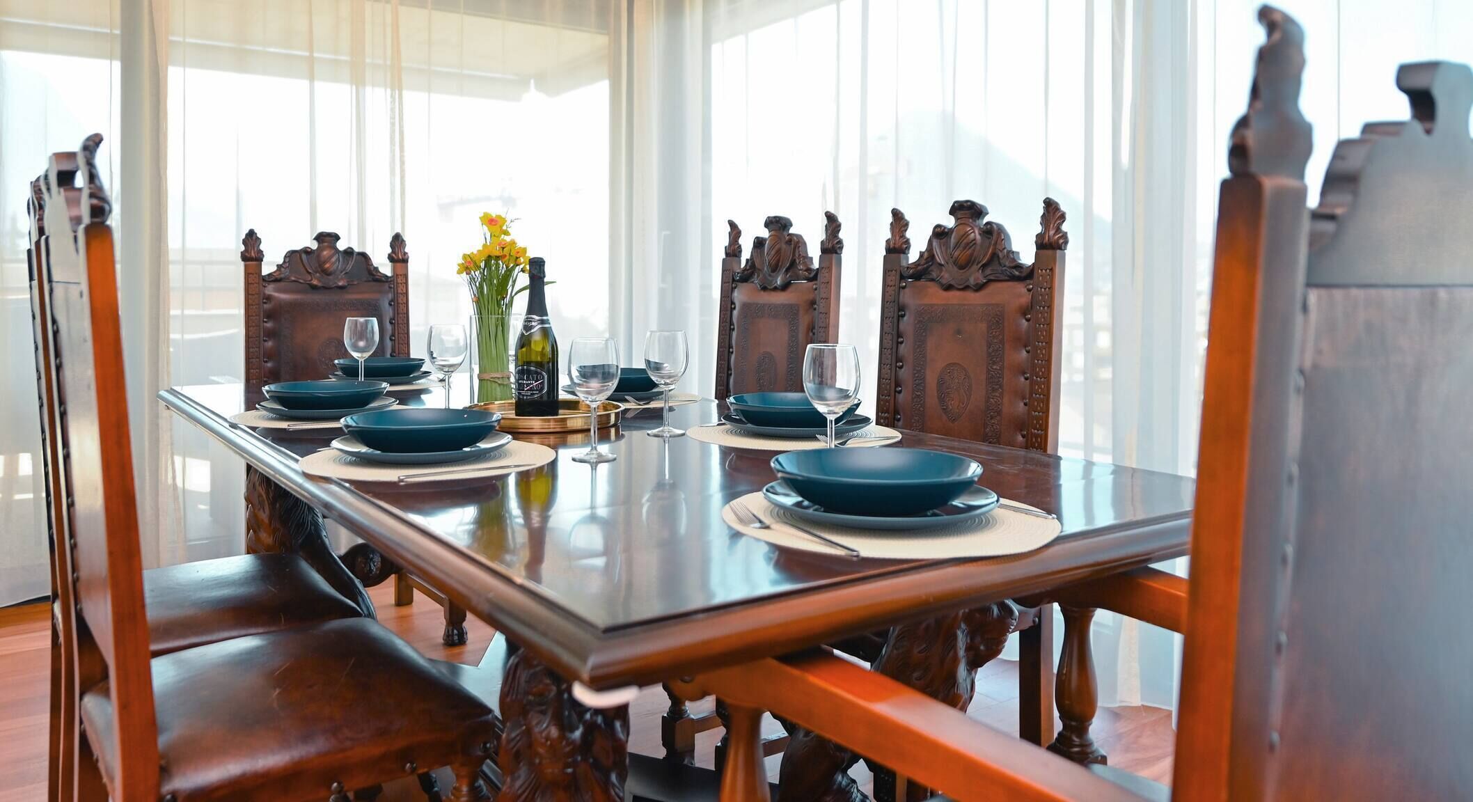 A dining table set for four with a bottle of wine, glasses, and a vase of flowers.