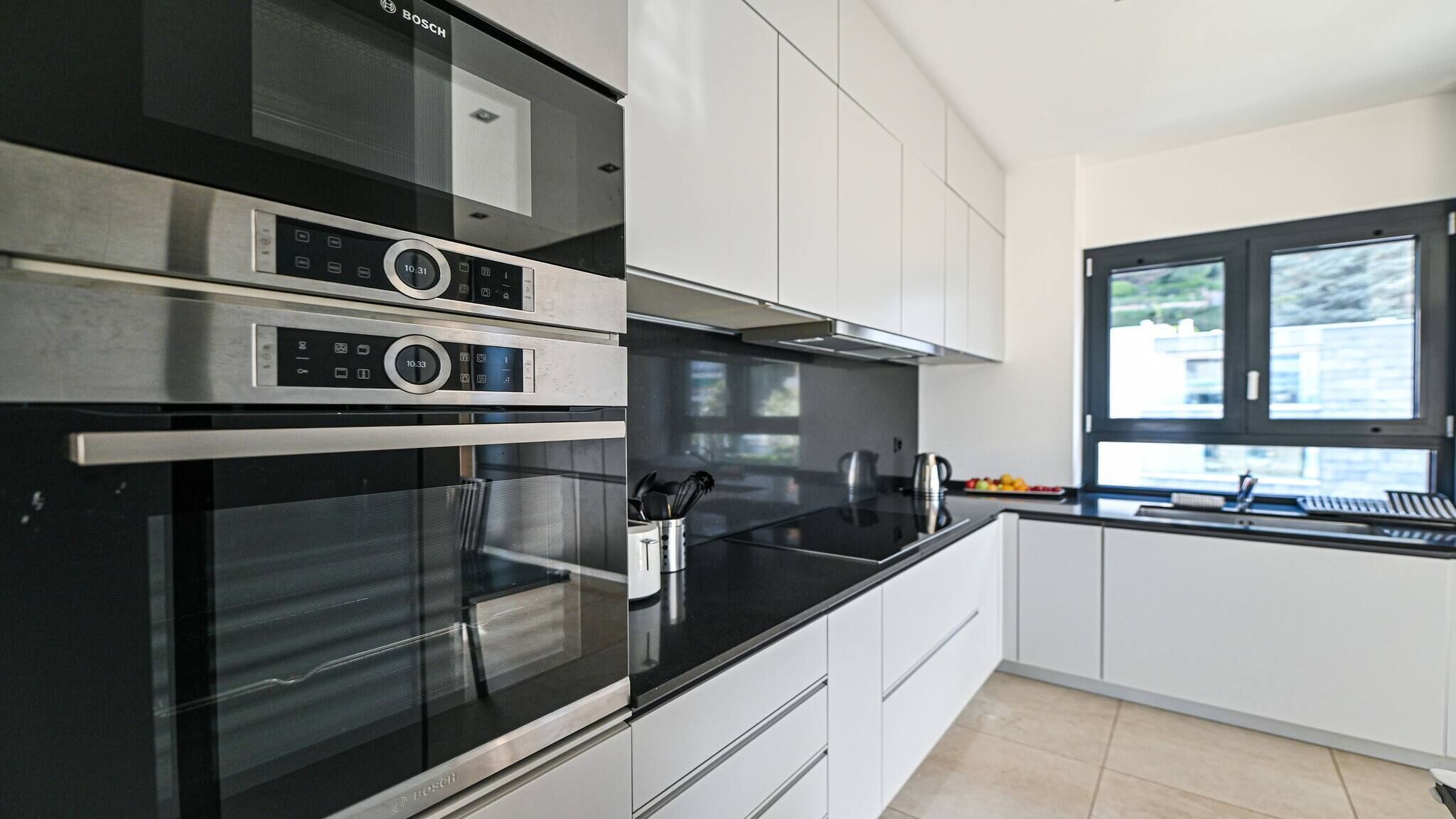 A modern kitchen with stainless steel appliances, white cabinetry, and a large window providing natural light.