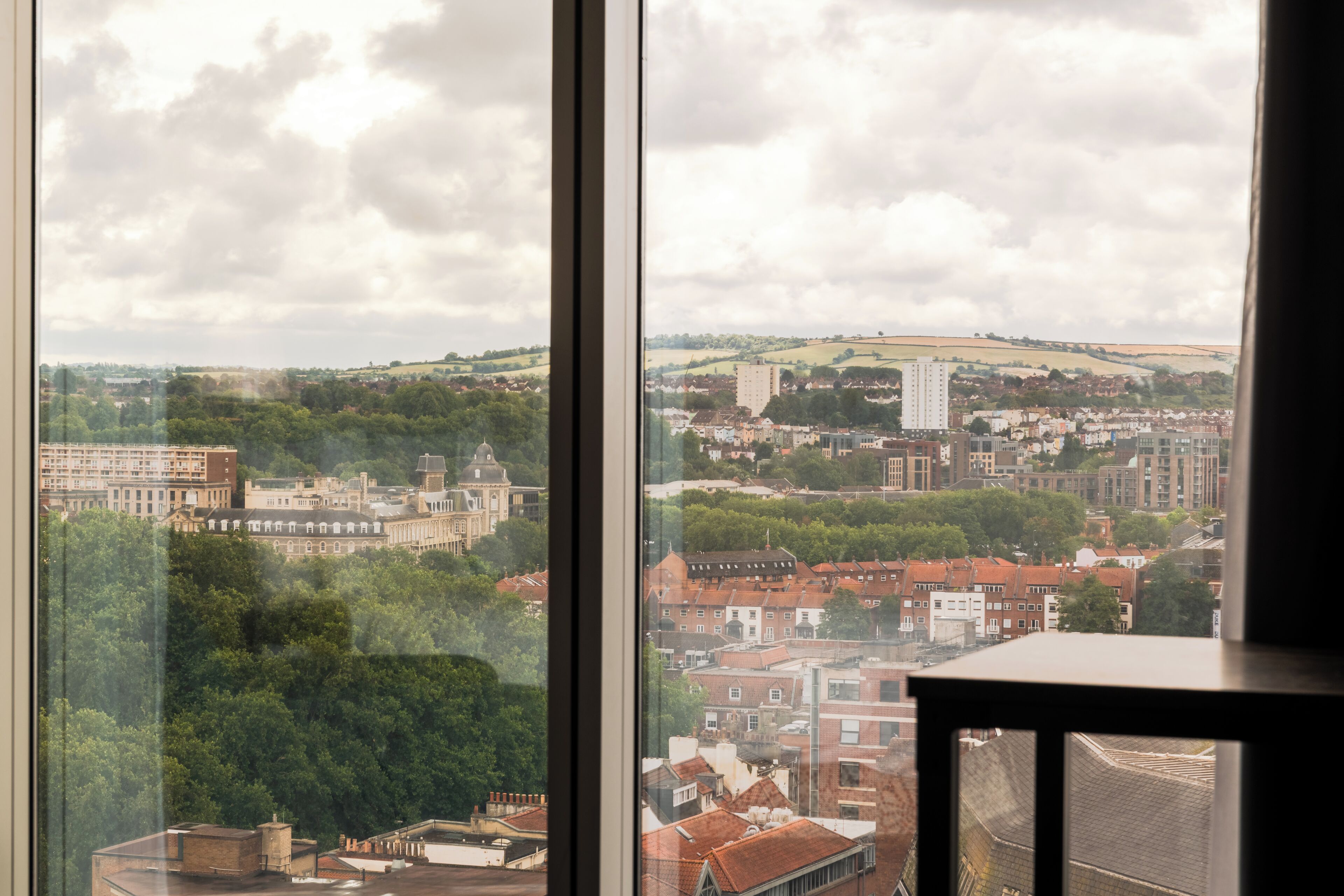 A cityscape through a window with buildings, trees, and a cloudy sky.