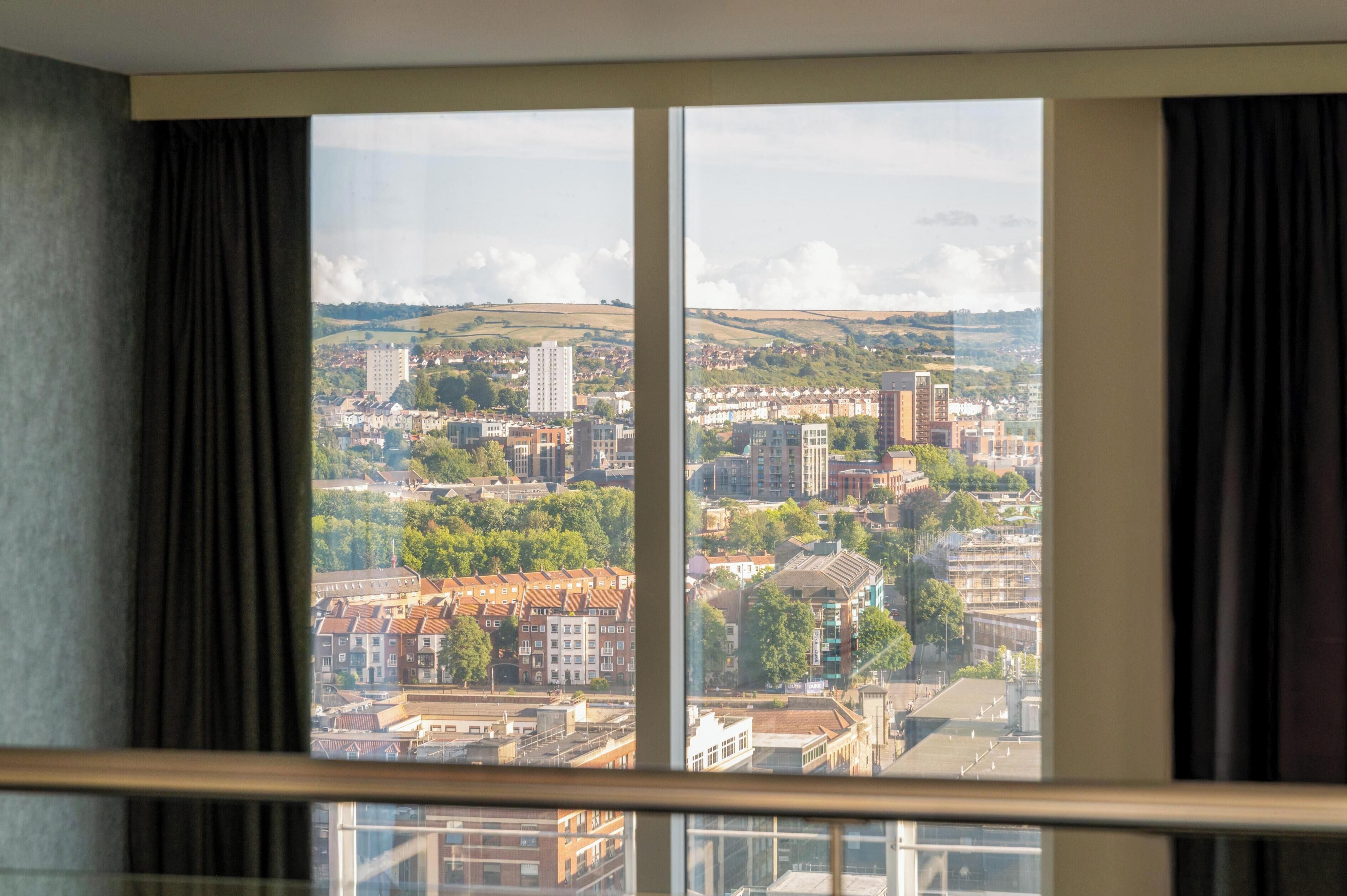 Una habitación con un ventanal amplio que ofrece vistas a un paisaje urbano con edificios y zonas verdes.