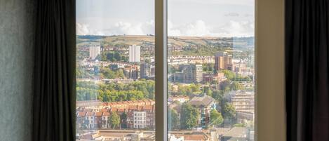 Una habitación con un ventanal amplio que ofrece vistas a un paisaje urbano con edificios y zonas verdes.