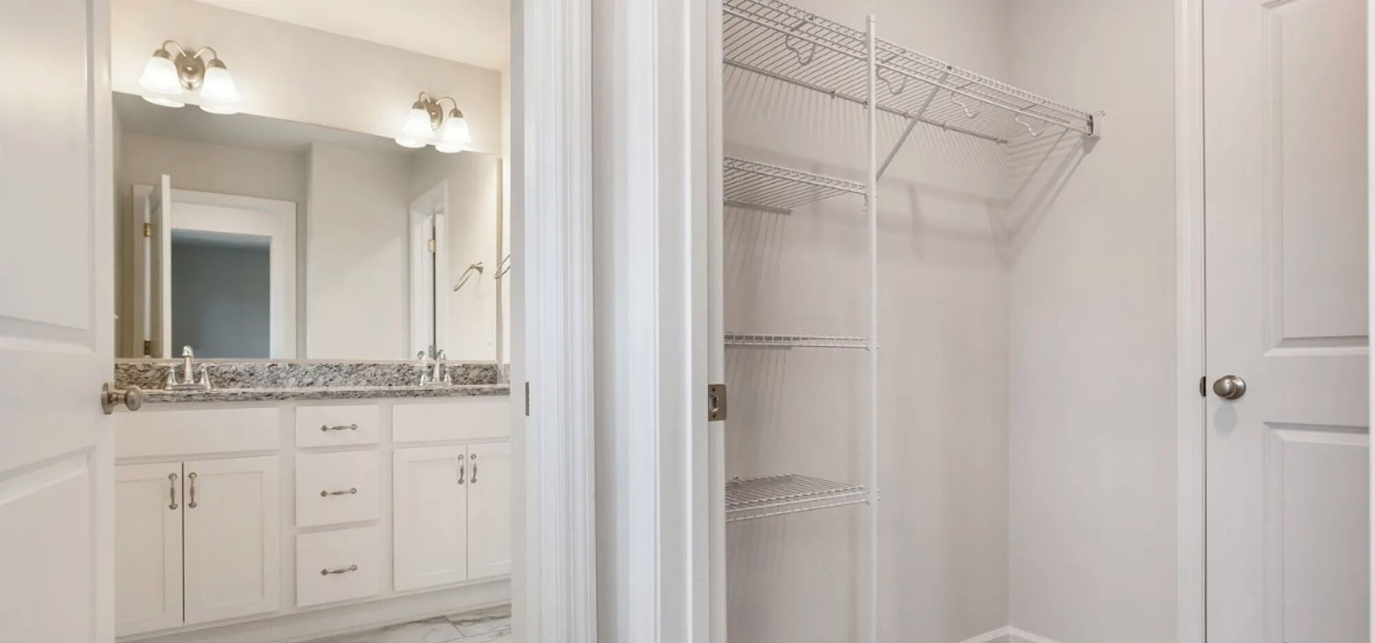 A bathroom with a vanity, a mirror, and a walk-in closet with shelves.