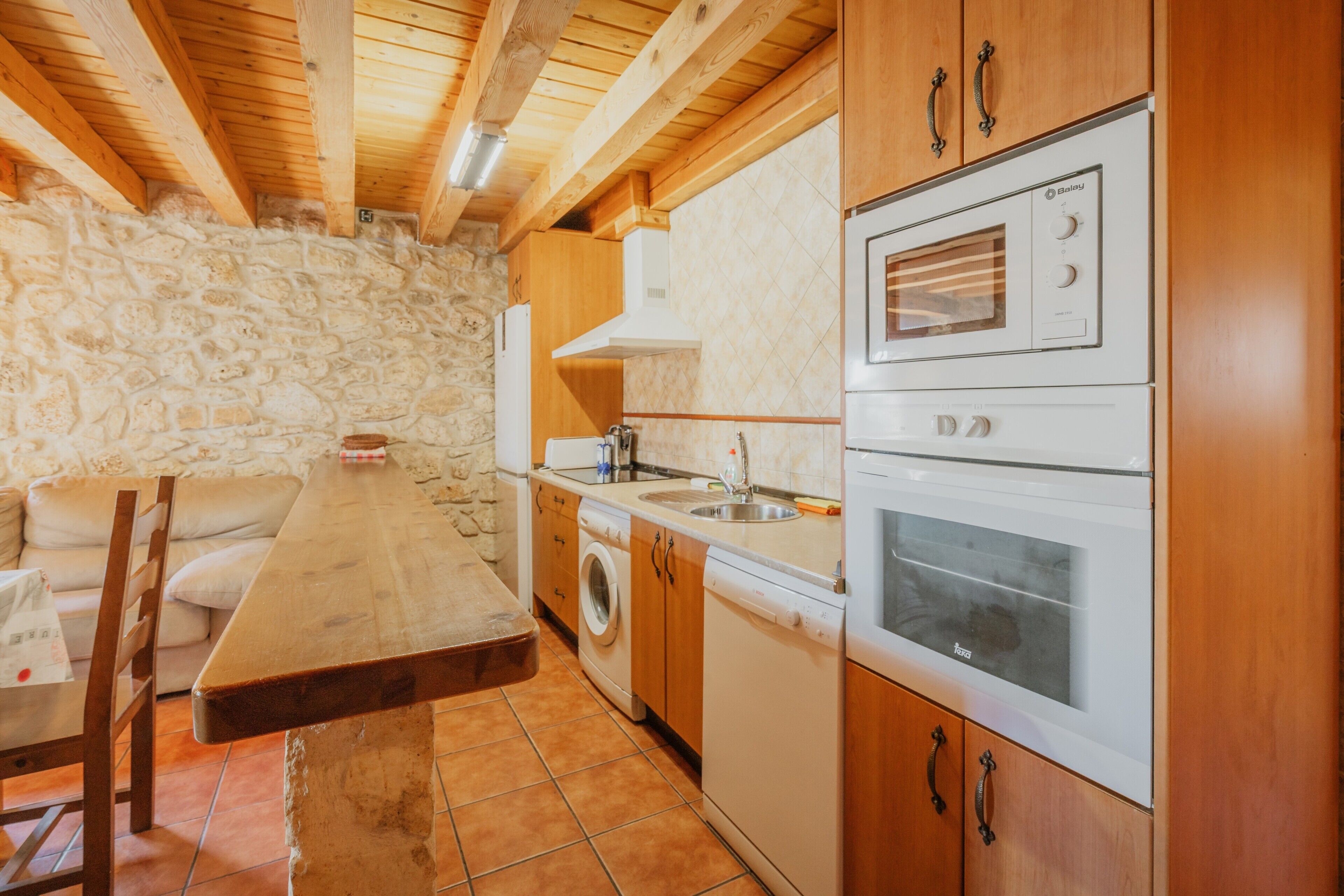A kitchen with stone walls, wooden cabinets, a built-in oven, and a washing machine.