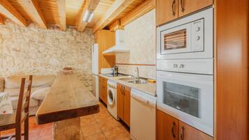 A kitchen with stone walls, wooden cabinets, a built-in oven, and a washing machine.