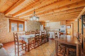 Ein Essbereich aus Holz mit einem großen Tisch und Stühlen, einer Steinwand und einer Küche im Hintergrund.