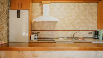 Una cucina con parete in pietra, mobili in legno, frigorifero bianco, lavello in acciaio inossidabile e zoccolo a mosaico.