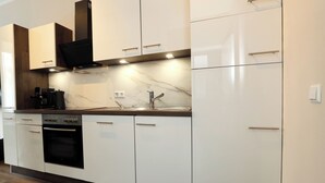 A modern kitchen with white cabinetry, a built-in oven, a marble countertop, and a black range hood. - ElbSuite 3 room apartment, 70sqm, old town and new town 10 minutes on foot (Dresden)