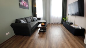 A modern living room with a sofa, a coffee table, a flat-screen TV, and a large window with curtains. - ElbSuite 3 room apartment, 70sqm, old town and new town 10 minutes on foot (Dresden)