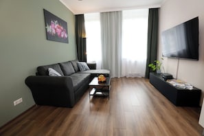 Ein modernes Wohnzimmer mit einer Couch, einem Couchtisch, einem Flachbildfernseher und einem großen Fenster mit Vorhängen.