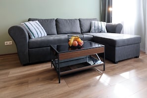 Ein modernes Wohnzimmer mit einem Ecksofa, einem Glastisch und einer Obstschale.