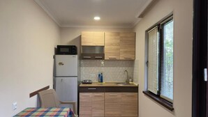 A compact kitchen with wooden cabinets, a microwave, a sink, and a window with blinds. - Hotel sataplia (Tsqaltubo)