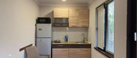 Una cocina compacta con armarios de madera, microondas, lavamanos y ventana con persianas.
