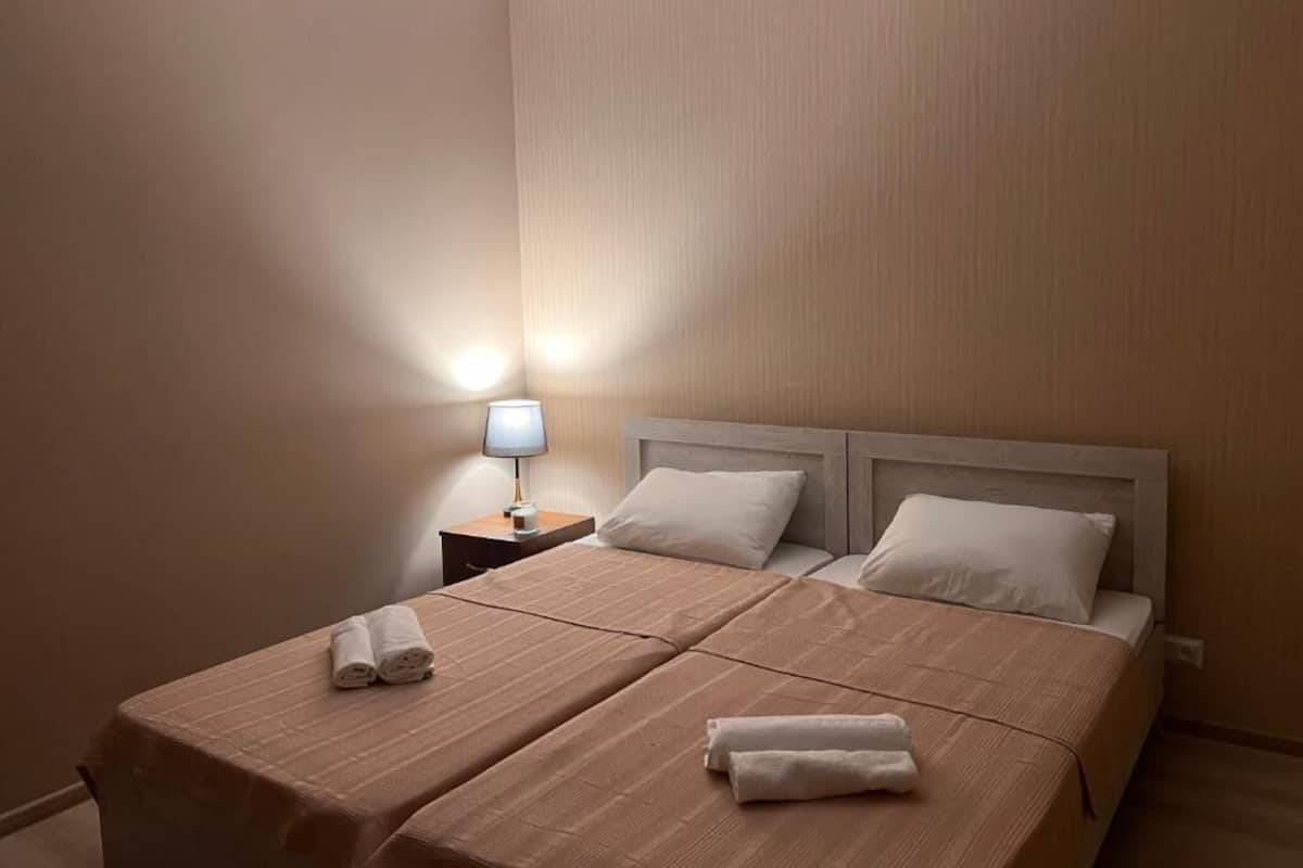 A hotel room with a double bed, a nightstand with a lamp, and a neatly made bed with towels.