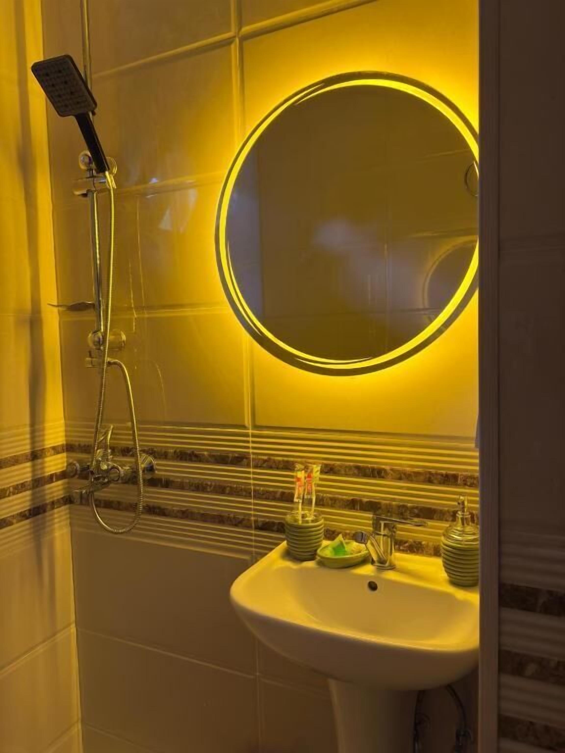Un baño con ducha, lavamanos y espejo con luz circular.