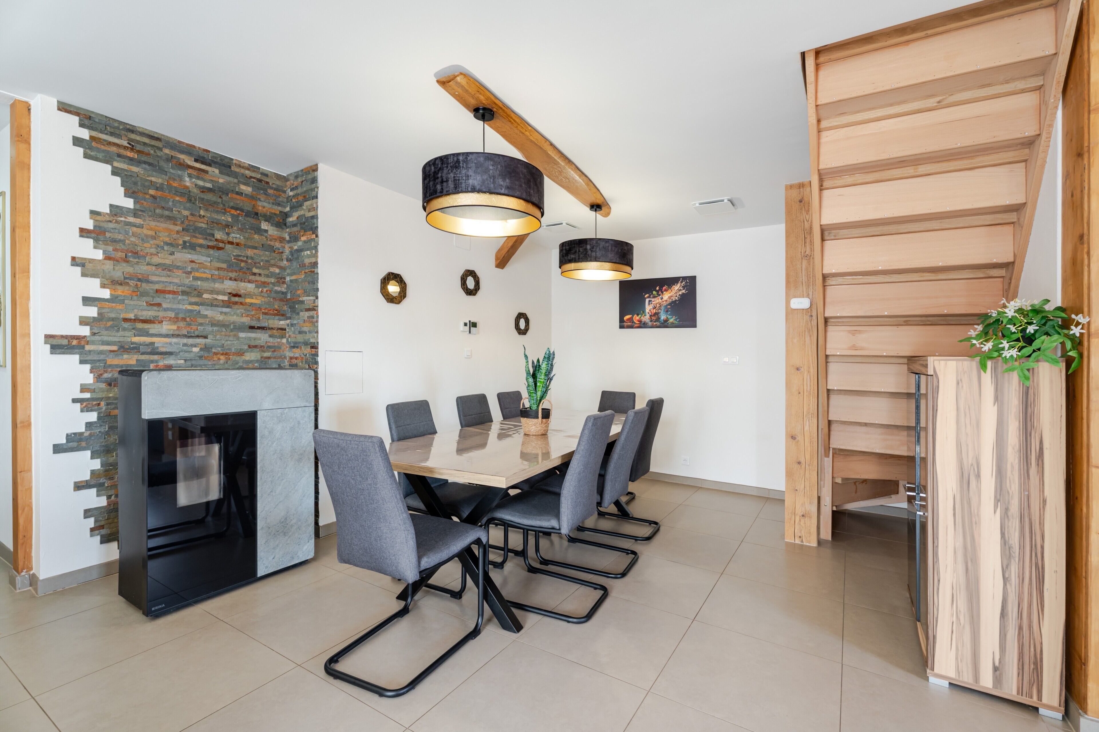 A modern dining area with a wooden table, grey chairs, a black-framed fireplace, and a stone wall.